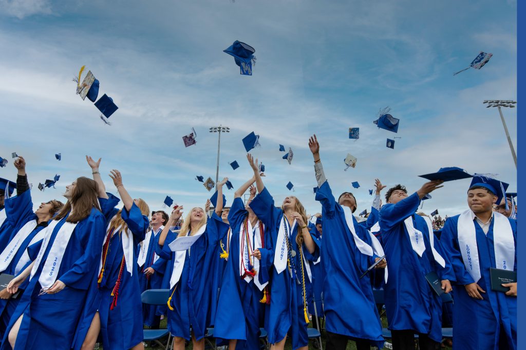 Graduates in blue caps and gowns joyfully toss their caps into the air during a graduation ceremony.